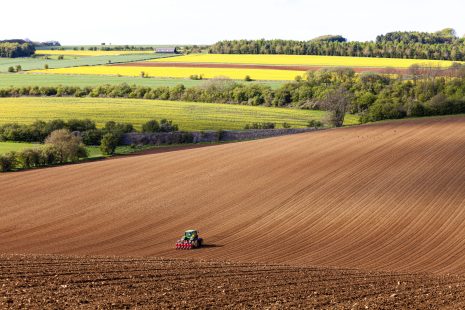 A tractor and seed drill sowing on Cotswold brash soil near the Cotswold village of Hampen, Gloucestershire UK