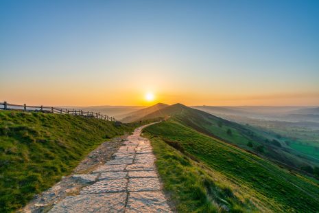 Impact storytelling Stone footpath and wooden fence leading along The Great Ridge in the English Peak District to the sun
